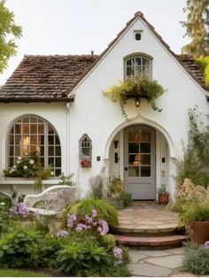 a white house with lots of plants and flowers around it's front entrance area