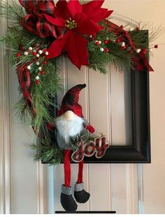 a christmas wreath hanging on the front door with an elf's hat and red poinsetti