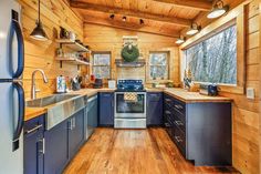 a kitchen with blue cabinets and stainless steel appliances in a log cabin style home on the edge of a forest