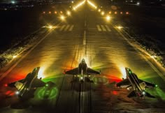 two fighter jets are parked on the runway at night with their lights turned green and red