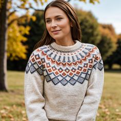 a woman standing in front of a tree wearing a sweater