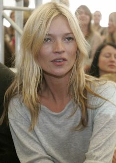 a woman with long blonde hair sitting in front of a group of people looking at the camera