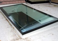 a flat glass window sitting on top of a white roof next to a brick building