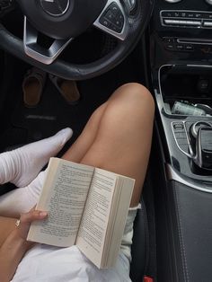 a woman is reading a book while sitting in the driver's seat of a car