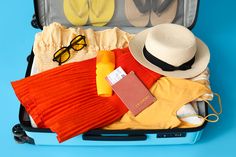 an open suitcase filled with clothing and accessories on a blue background next to flip flops