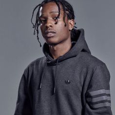 a man with dreadlocks standing in front of a gray background wearing a black hoodie