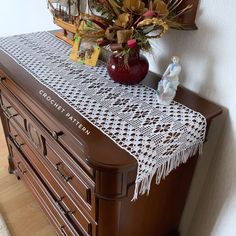 a crocheted lace table runner sits on top of an old dresser with a vase full of flowers