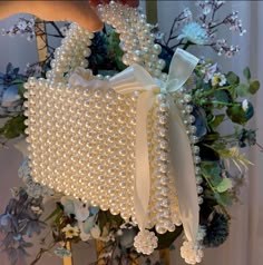 a white purse with pearls on it sitting next to flowers