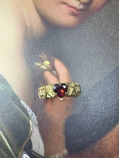 a close up of a person's hand holding a ring with a red stone