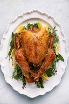 a whole chicken on a plate with lemons and herbs