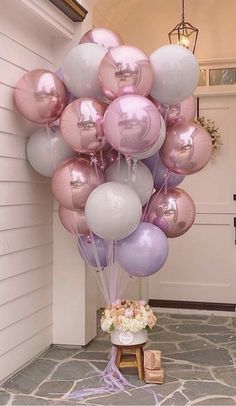 a bunch of balloons that are on the ground in front of a house with flowers