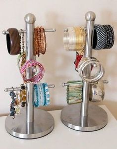 two metal racks holding bracelets and rings on top of each other in front of a white wall