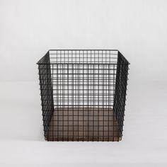 a black wire basket sitting on top of a wooden floor in front of a white wall