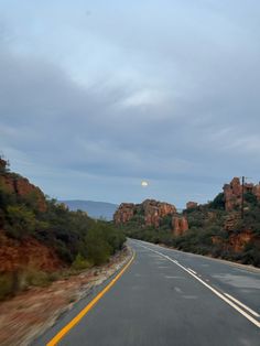 an empty road with trees and mountains in the background at dusk or dawn, as seen from a moving vehicle