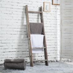 a wooden ladder leaning against a white brick wall with towels on the floor next to it