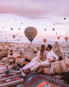 two people sitting on a couch with hot air balloons in the background