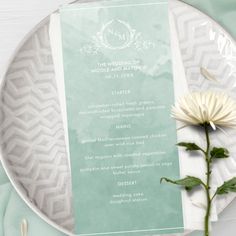 a white flower sitting on top of a plate next to a green menu cover and napkin