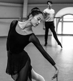 two ballerinas are in the middle of a dance class, one is wearing a black leotard