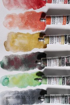 six different colors of watercolor paint on white paper