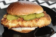 a fried chicken sandwich with pickles on a black plate