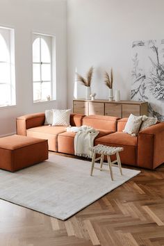 a living room with an orange couch and white rugs on the wooden flooring