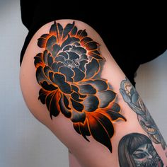 a woman's thigh with an orange and black flower tattoo design on her leg