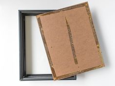 two pieces of cardboard sitting in front of a black frame on a white wall,