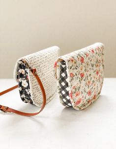 two purses sitting next to each other on a white counter top, one has a flowered design and the other has a brown leather strap