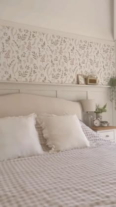 a bed with white sheets and pillows in a bedroom next to a wallpapered headboard