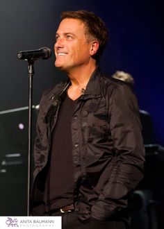 a man standing in front of a microphone on top of a stage with another person behind him