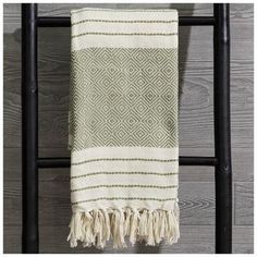 a white and green towel hanging on a black rack next to a wooden wall with an old ladder