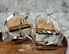 two sandwiches wrapped in plastic sitting on top of a wooden board