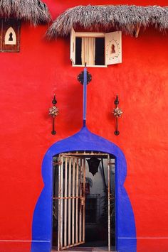 a red building with a blue door and thatched roof over the entrance to it