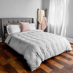 a bed sitting on top of a hard wood floor next to a window with white curtains