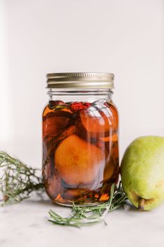 a glass jar filled with liquid next to an apple and sprig of rosemary