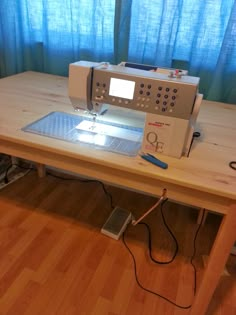 a sewing machine sitting on top of a wooden table in front of a window with blue curtains