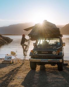 a man standing on top of a ladder next to a parked vehicle near the water