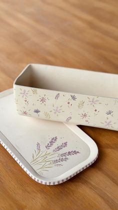 two white dishes sitting on top of a wooden table next to each other with flowers painted on them