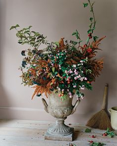 a vase filled with lots of flowers on top of a wooden floor next to a broom