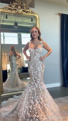 a woman standing in front of a mirror wearing a wedding dress with flowers on it