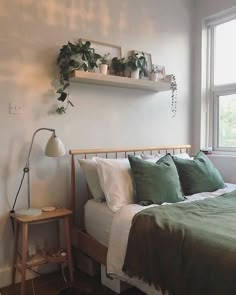 a bedroom with white walls and green bedding, potted plants on the wall