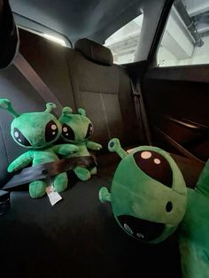 two stuffed animals sit in the back seat of a car, one is green and the other is black