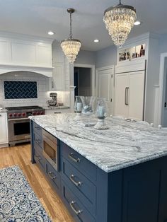 a large kitchen island with marble counter tops and blue cabinets in the center is flanked by two crystal chandeliers