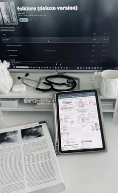 a tablet computer sitting on top of a desk next to a book and cup with a stethoscope