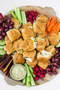 a platter filled with rolls, carrots, celery, grapes and dip