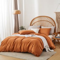 a bed with orange sheets and pillows in a room next to a wicker headboard