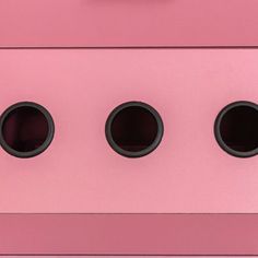 three round holes in the side of a pink cabinet with black knobs on it