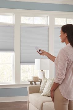 a woman standing in front of a window holding a remote control and pointing at the blinds