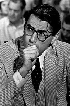 black and white photograph of man in suit sitting at desk with papers, reading glasses