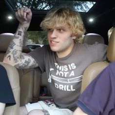 a young man sitting in the back seat of a car with tattoos on his arm